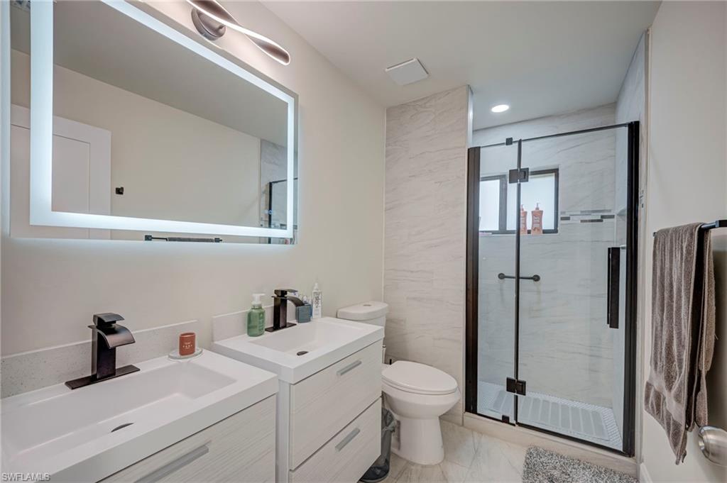 Bathroom featuring two vanities and a marble finish shower
