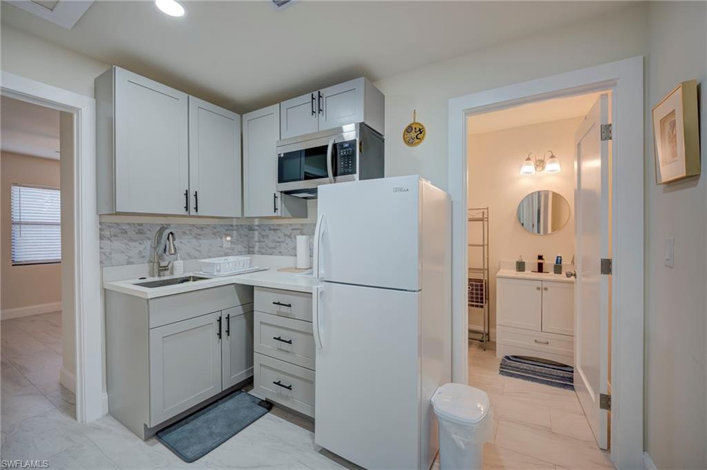 Kitchen featuring freestanding refrigerator, light countertops, stainless steel microwave, light marble finish floors, and decorative backsplash