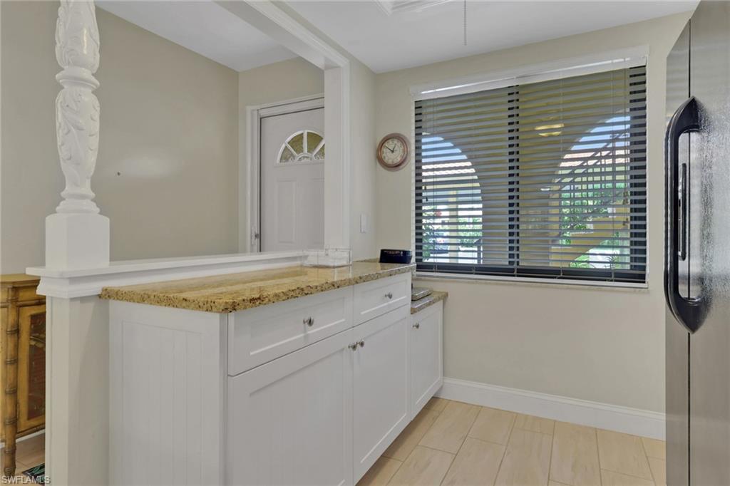 Kitchen featuring freestanding refrigerator, a peninsula, light stone countertops, and white cabinetry