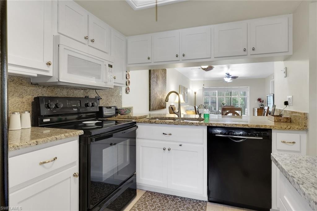 Kitchen with black appliances, white cabinets, decorative backsplash, and light stone counters