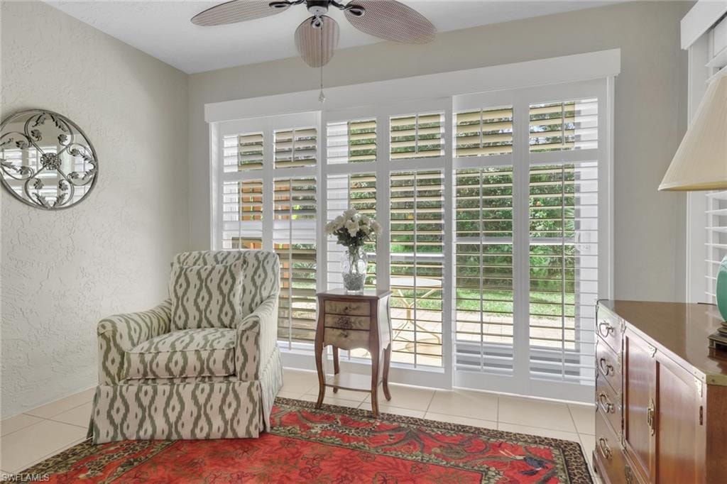Sitting room with a textured wall, light tile patterned flooring, and a ceiling fan