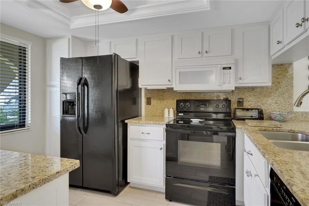 Kitchen featuring black appliances, white cabinetry, light stone countertops, a tray ceiling, and ornamental molding