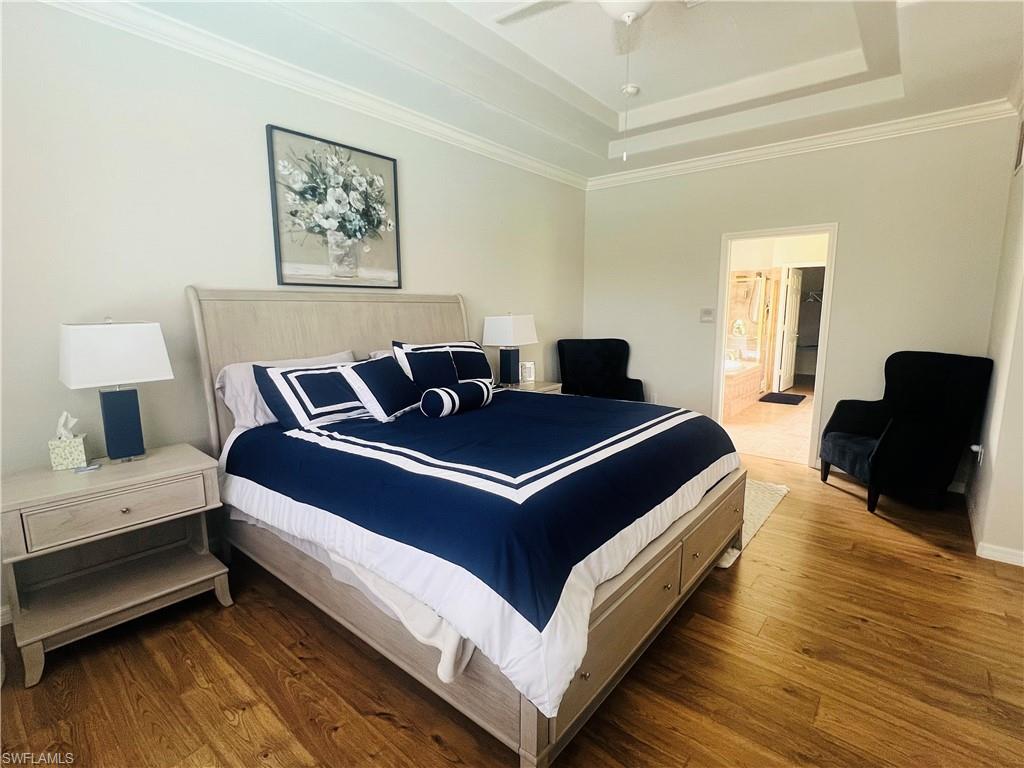 Bedroom with ensuite bath, a raised ceiling, ceiling fan, wood-type flooring, and ornamental molding