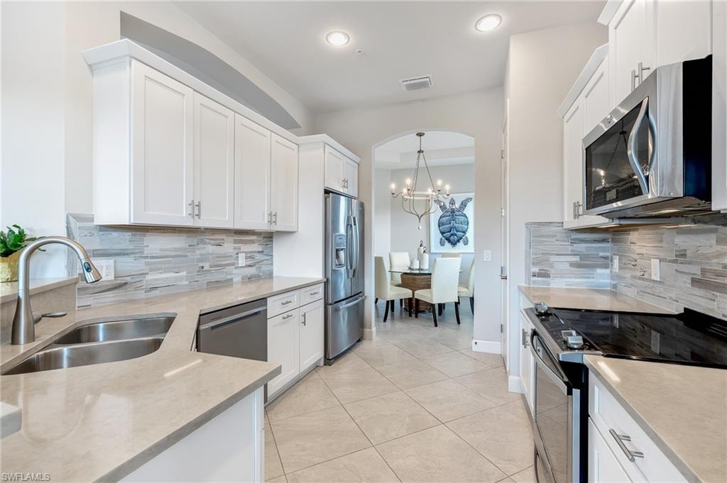 Kitchen with white cabinets, stainless steel appliances, light stone countertops, light tile patterned floors, and a chandelier