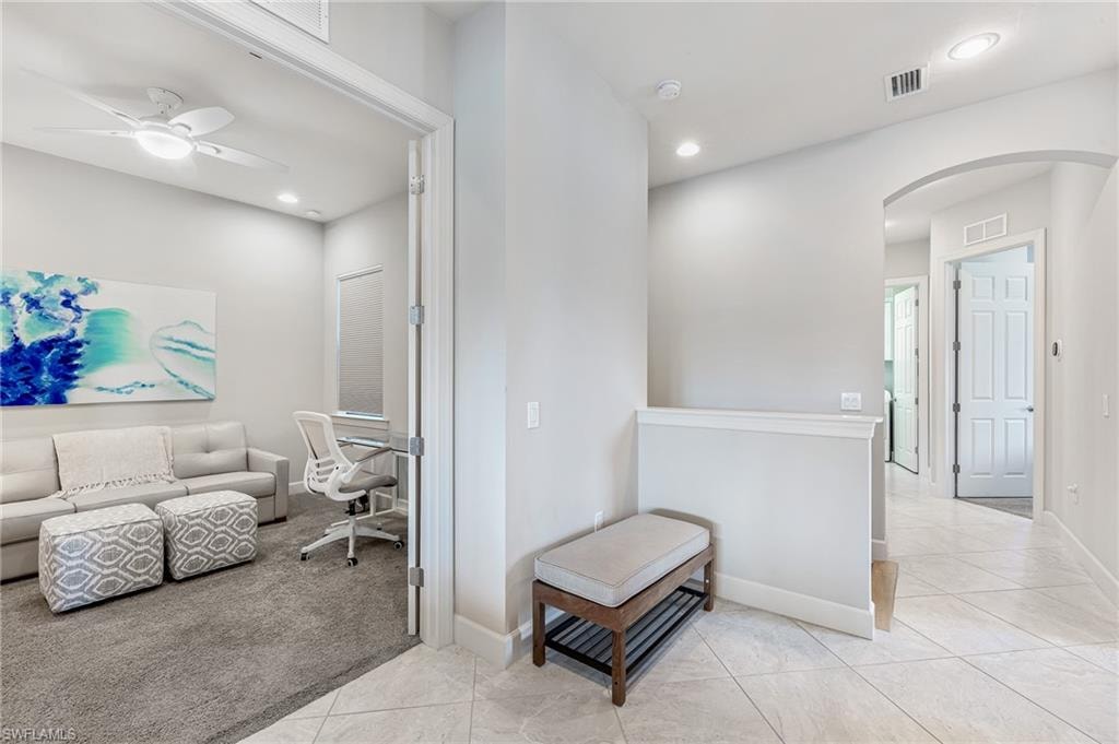 Hallway featuring arched walkways, light colored carpet, light tile patterned flooring, recessed lighting, and a desk