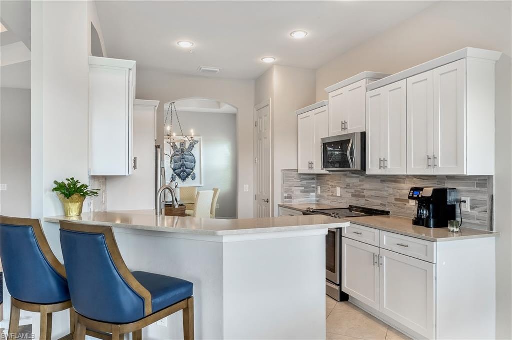 Kitchen featuring white cabinets, a kitchen bar, stainless steel appliances, a peninsula, and tasteful backsplash