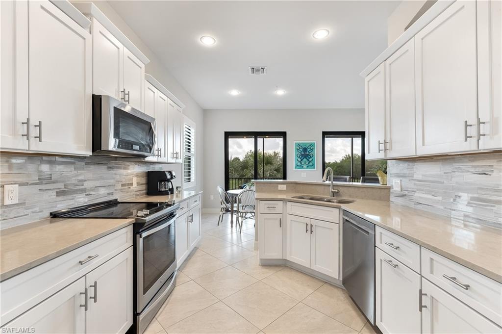 Kitchen featuring decorative backsplash, stainless steel appliances, a peninsula, white cabinets, and light tile patterned flooring