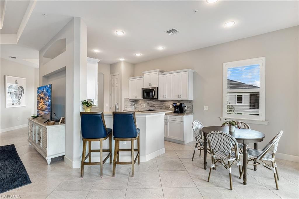 Kitchen featuring white cabinets, light countertops, a breakfast bar, decorative backsplash, and stainless steel microwave