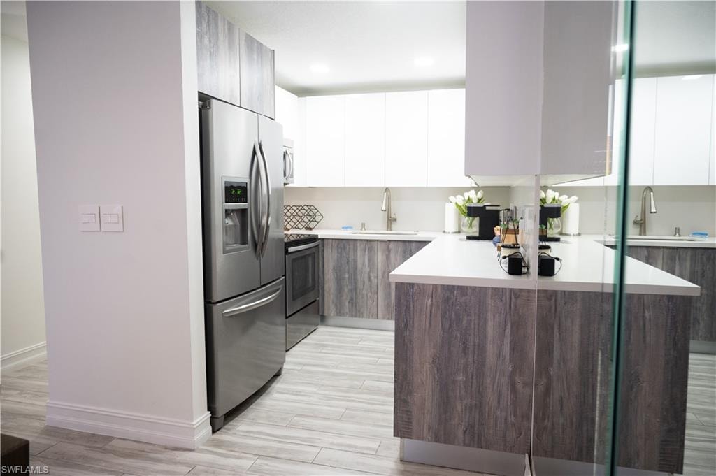 Kitchen featuring dual tone cabinetry, modern cabinets, stainless steel appliances, wood tiled floors, and recessed lighting
