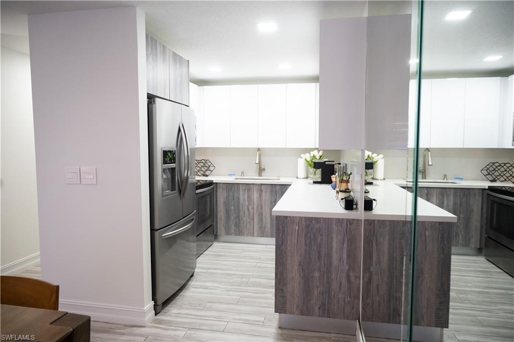 Dual tone kitchen with dual tone cabinetry, modern cabinets, stainless steel appliances, wood finish floors, and light stone countertops