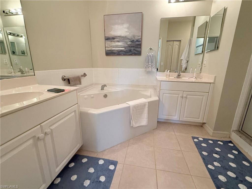 Full bath featuring light tile patterned flooring, two vanities, and a garden tub