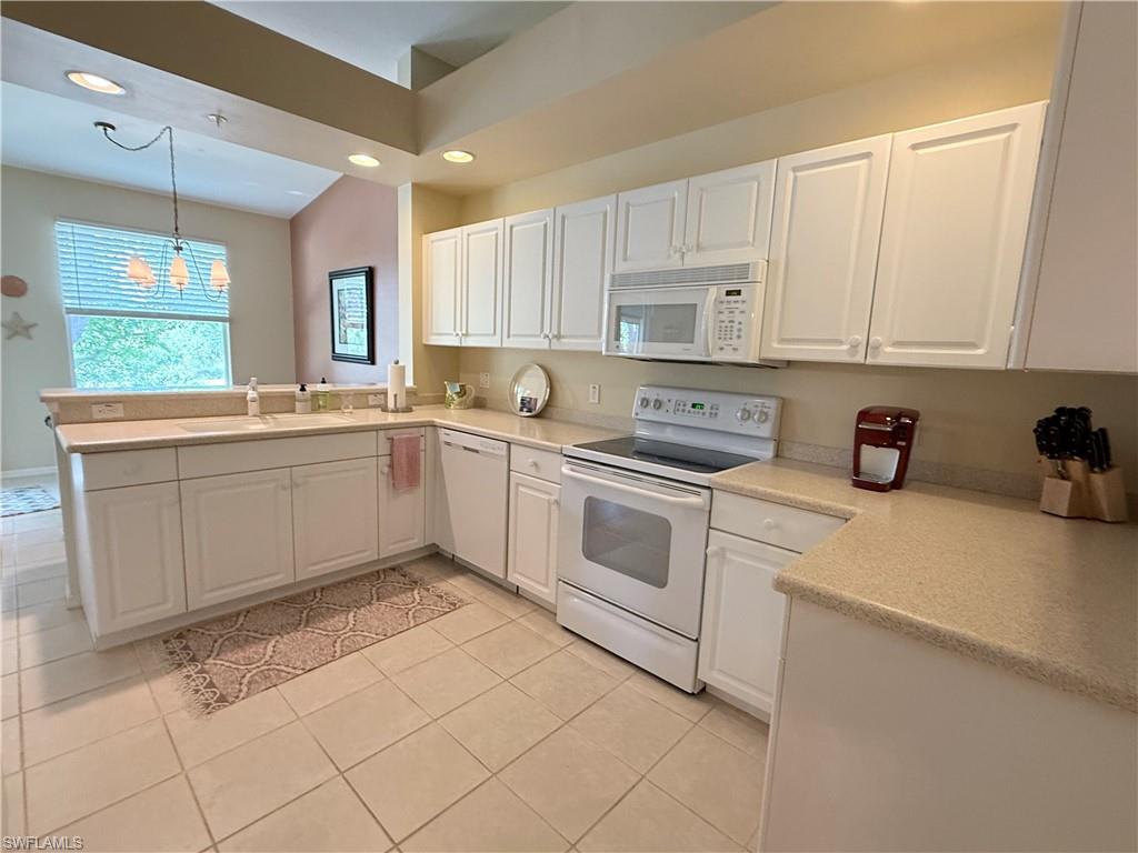 Kitchen featuring white appliances, white cabinets, a peninsula, decorative light fixtures, and light tile patterned floors
