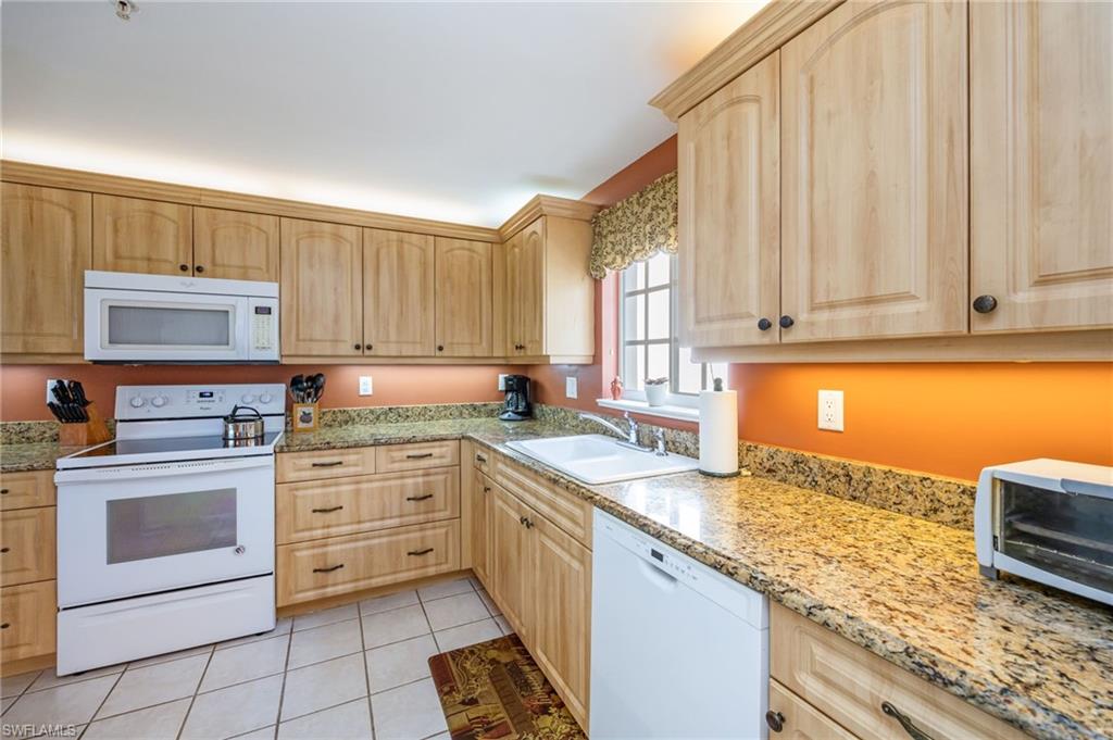 Kitchen with light wood finish cabinets, white appliances, light stone counters, and light tile patterned floors