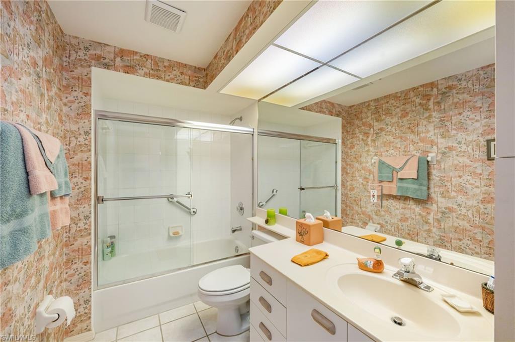 Full bathroom with wallpapered walls, vanity, enclosed tub / shower combo, and light tile patterned floors