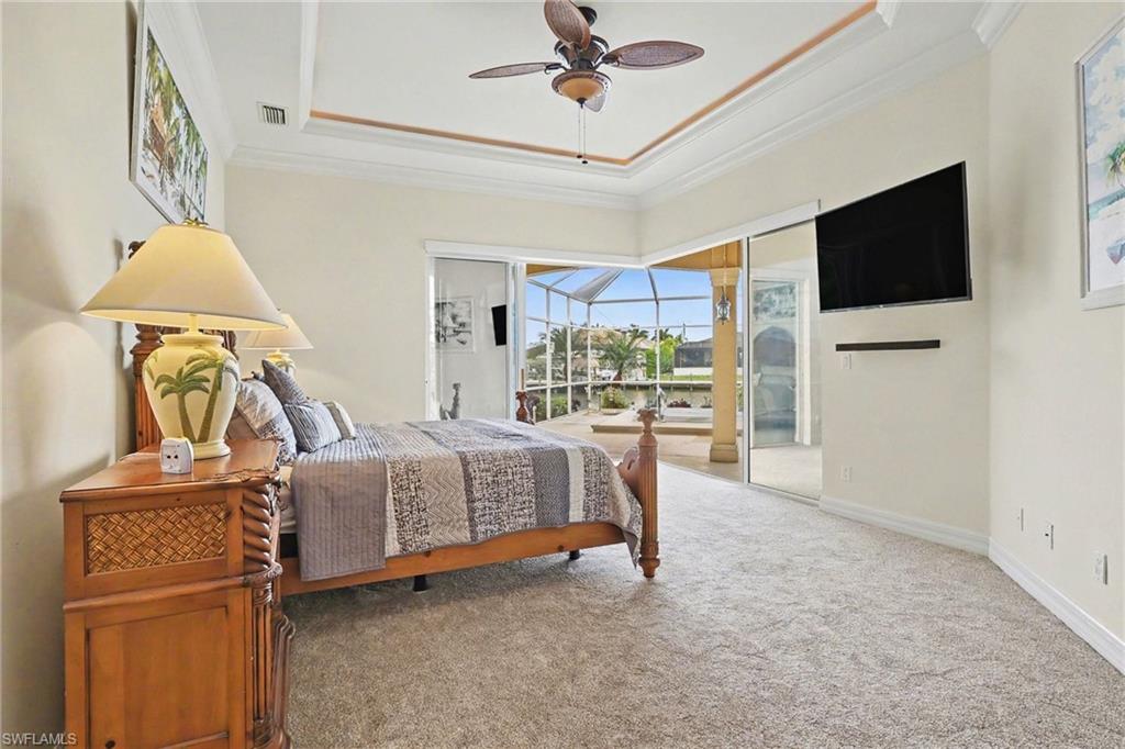 Carpeted bedroom with a sunroom, access to outside, ceiling fan, a tray ceiling, and ornamental molding