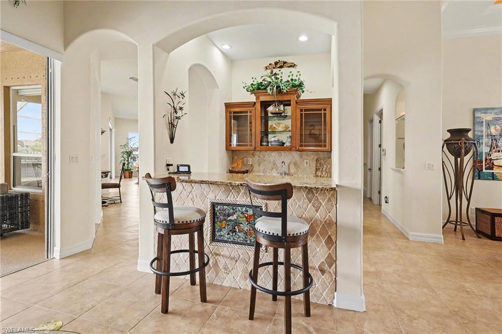 Indoor bar with glass fronted cabinets, wood finish cabinets, decorative backsplash, light stone counters, and arched walkways