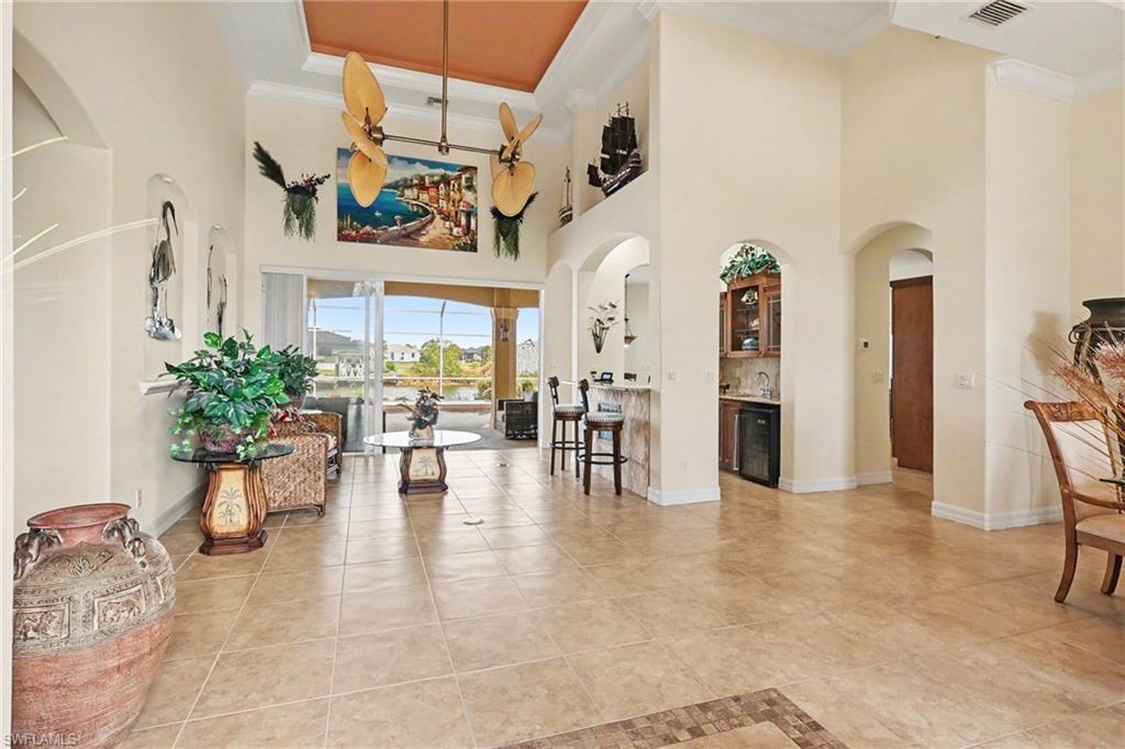 Foyer entrance with arched walkways, a high ceiling, crown molding, light tile patterned floors, and beverage cooler