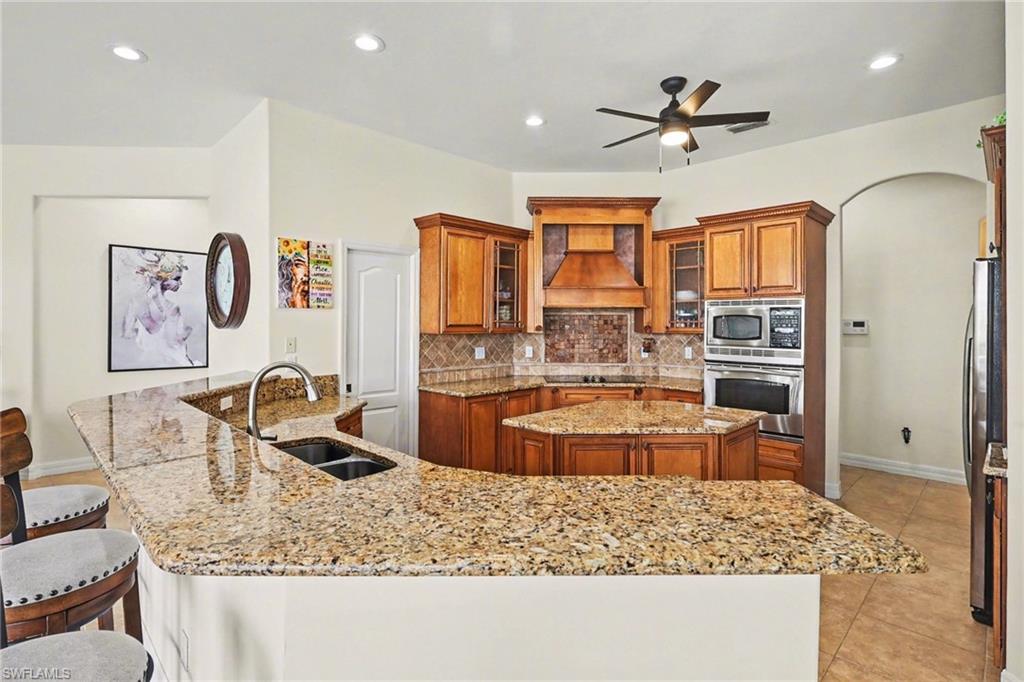 Kitchen featuring wood finish cabinetry, a kitchen bar, stainless steel appliances, arched walkways, and light stone countertops