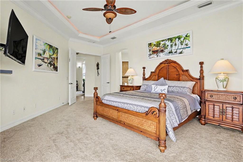 Bedroom with ornamental molding, light colored carpet, a ceiling fan, and a raised ceiling