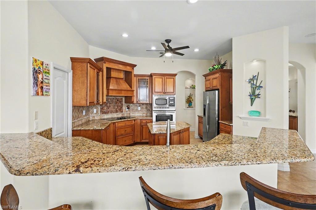 Kitchen with arched walkways, wood finish cabinetry, a breakfast bar, a peninsula, and decorative backsplash