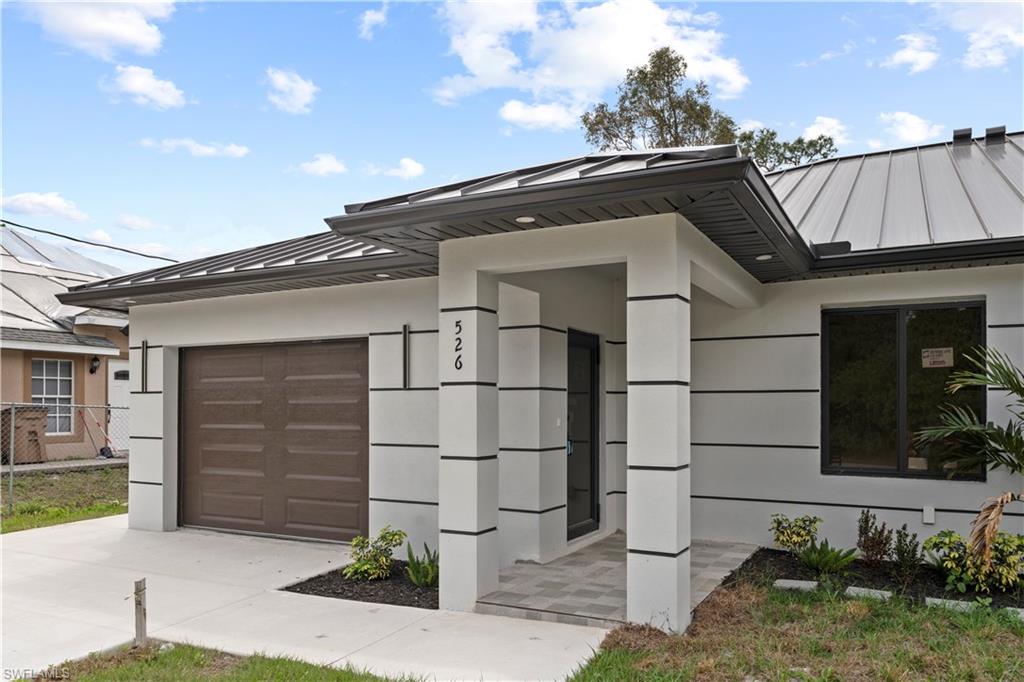 View of front facade featuring a standing seam roof, stucco siding, an attached garage, and concrete driveway