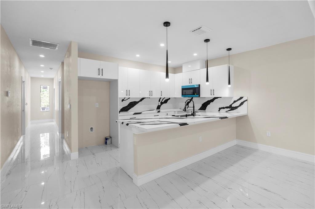 Kitchen with a peninsula, light marble finish floors, stainless steel microwave, pendant lighting, and white cabinets