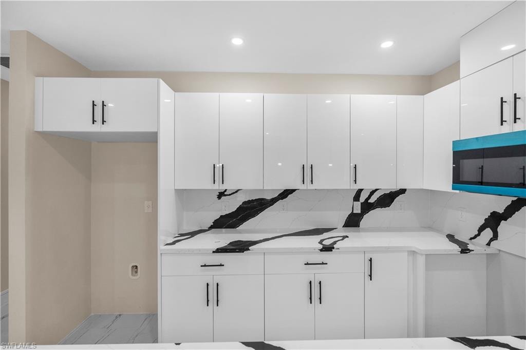 Kitchen featuring stainless steel microwave, white cabinets, backsplash, light stone counters, and modern cabinets