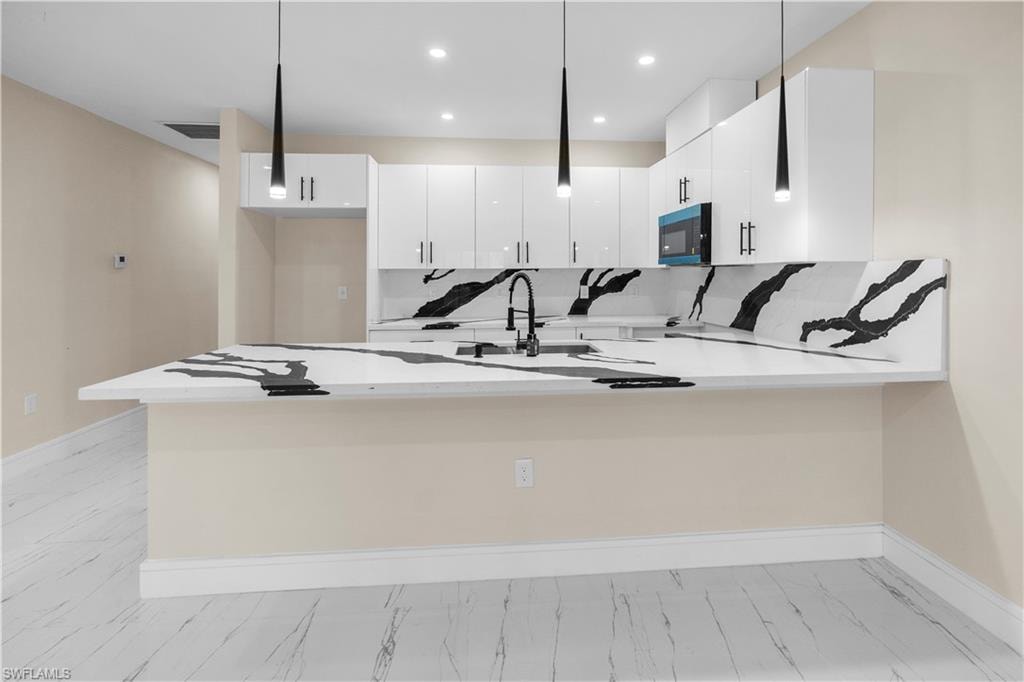 Kitchen featuring a peninsula, pendant lighting, white cabinets, light stone counters, and a breakfast bar area