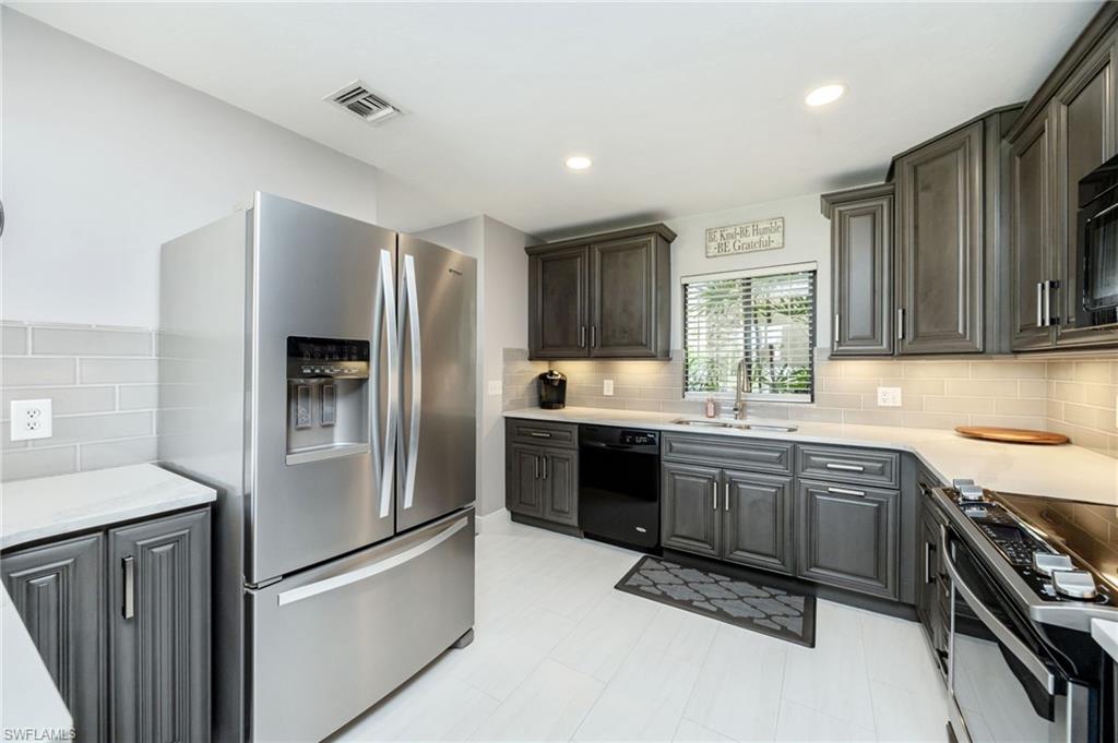 Kitchen with black appliances, light stone counters, recessed lighting, decorative backsplash, and gray cabinets
