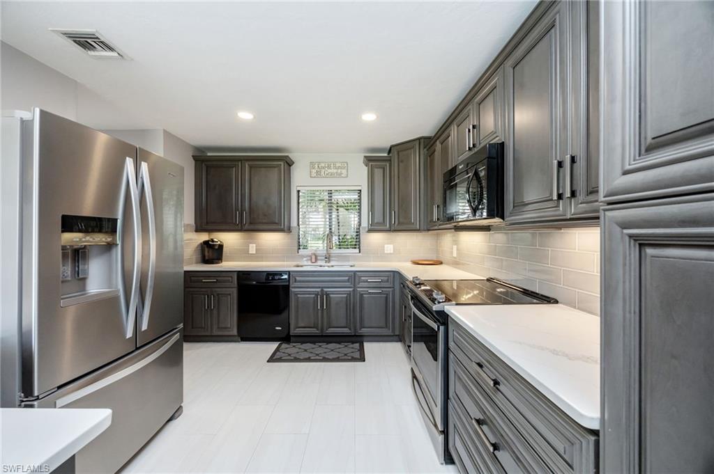 Kitchen featuring black appliances, backsplash, recessed lighting, gray cabinets, and light stone countertops