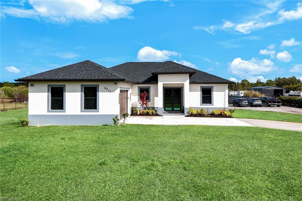 Prairie-style home with a front yard, stucco siding, and a shingled roof