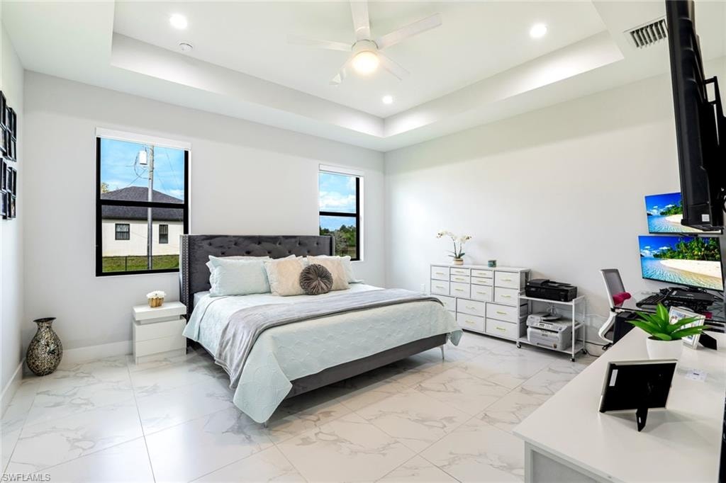 Bedroom with light marble finish flooring, ceiling fan, recessed lighting, and a tray ceiling