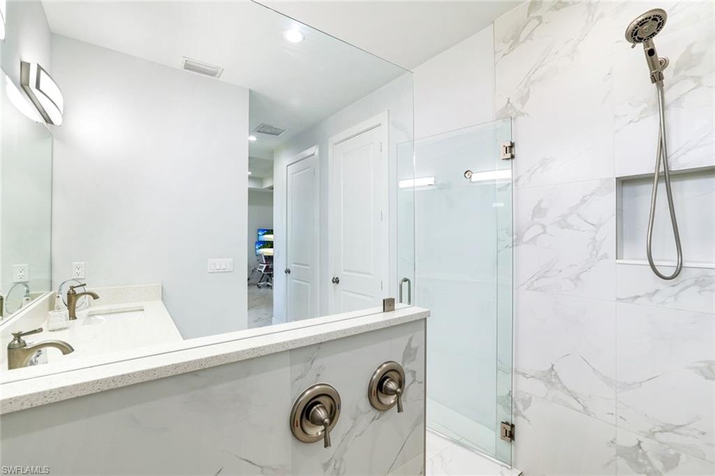 Full bath with double vanity, a marble finish shower, and recessed lighting