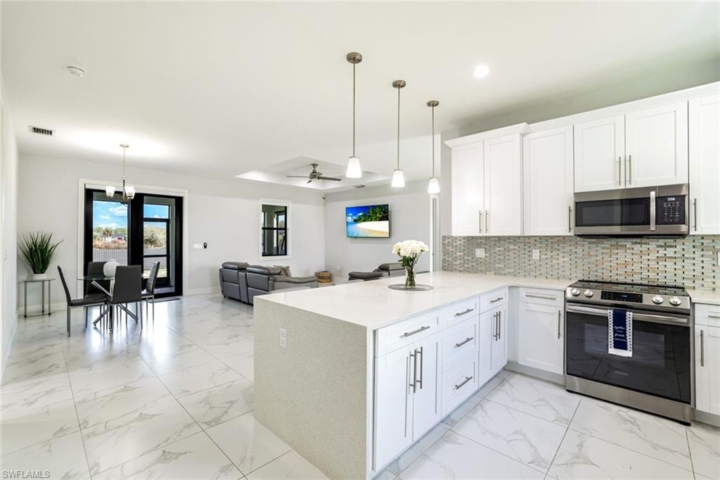Kitchen with stainless steel appliances, open floor plan, light marble finish floors, white cabinetry, and tasteful backsplash