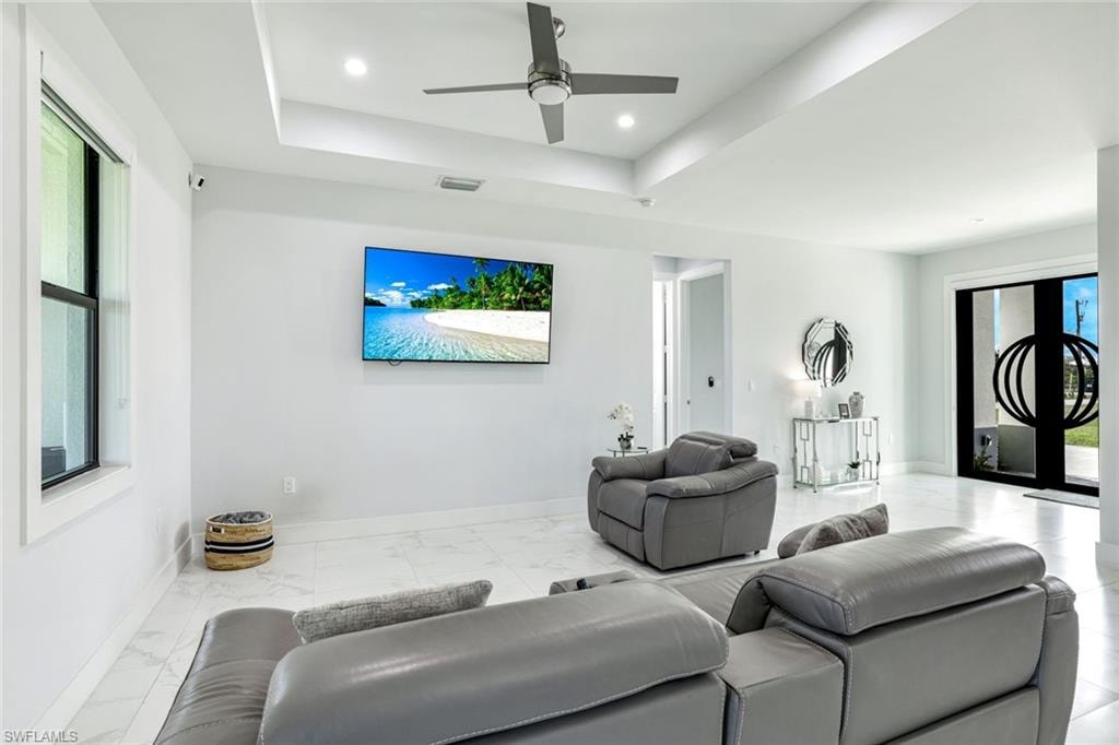 Living area with ceiling fan, a raised ceiling, light marble finish floors, and recessed lighting