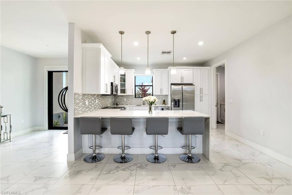 Kitchen with a peninsula, stainless steel appliances, a breakfast bar area, hanging light fixtures, and white cabinetry
