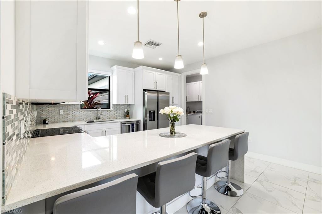 Kitchen with a peninsula, a kitchen bar, light stone countertops, stainless steel appliances, and white cabinetry