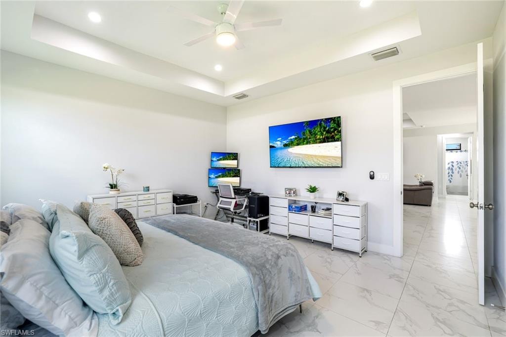 Bedroom featuring a tray ceiling, recessed lighting, ceiling fan, and light marble finish flooring