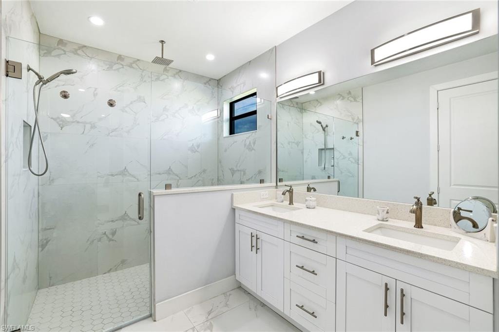 Bathroom featuring double vanity, a marble finish shower, and light marble finish floors