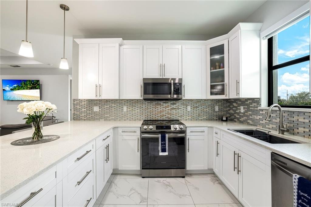 Kitchen featuring stainless steel appliances, white cabinetry, light marble finish flooring, light stone countertops, and decorative light fixtures