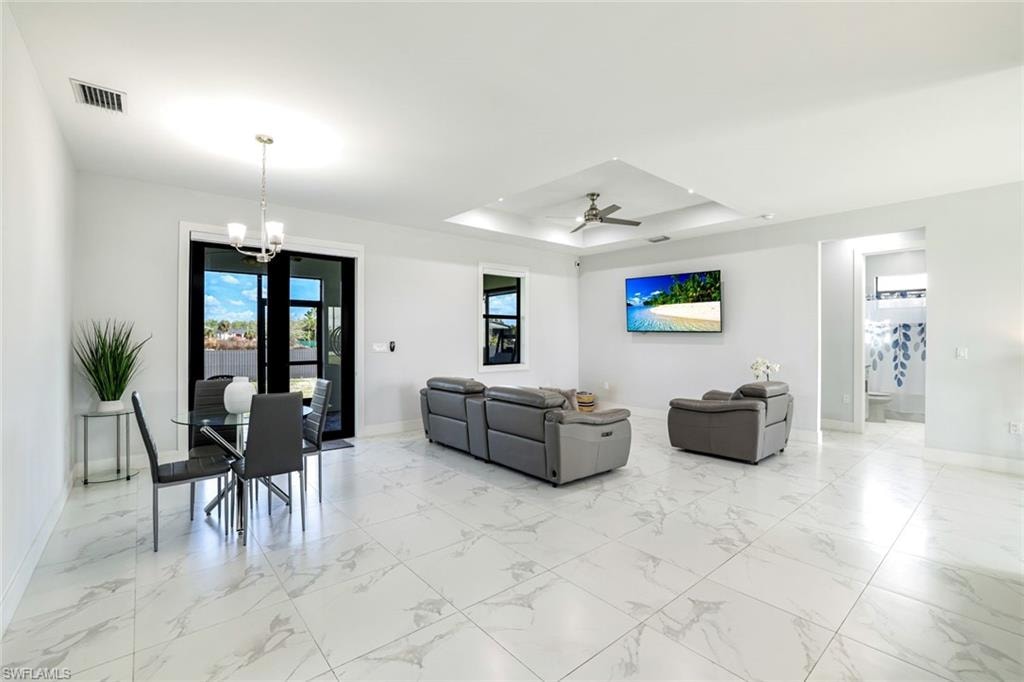Living room with ceiling fan, a chandelier, a tray ceiling, and light marble finish flooring