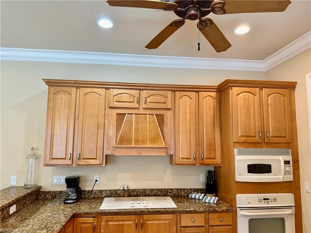 Kitchen featuring white appliances, ceiling fan, dark stone countertops, ornamental molding, and recessed lighting