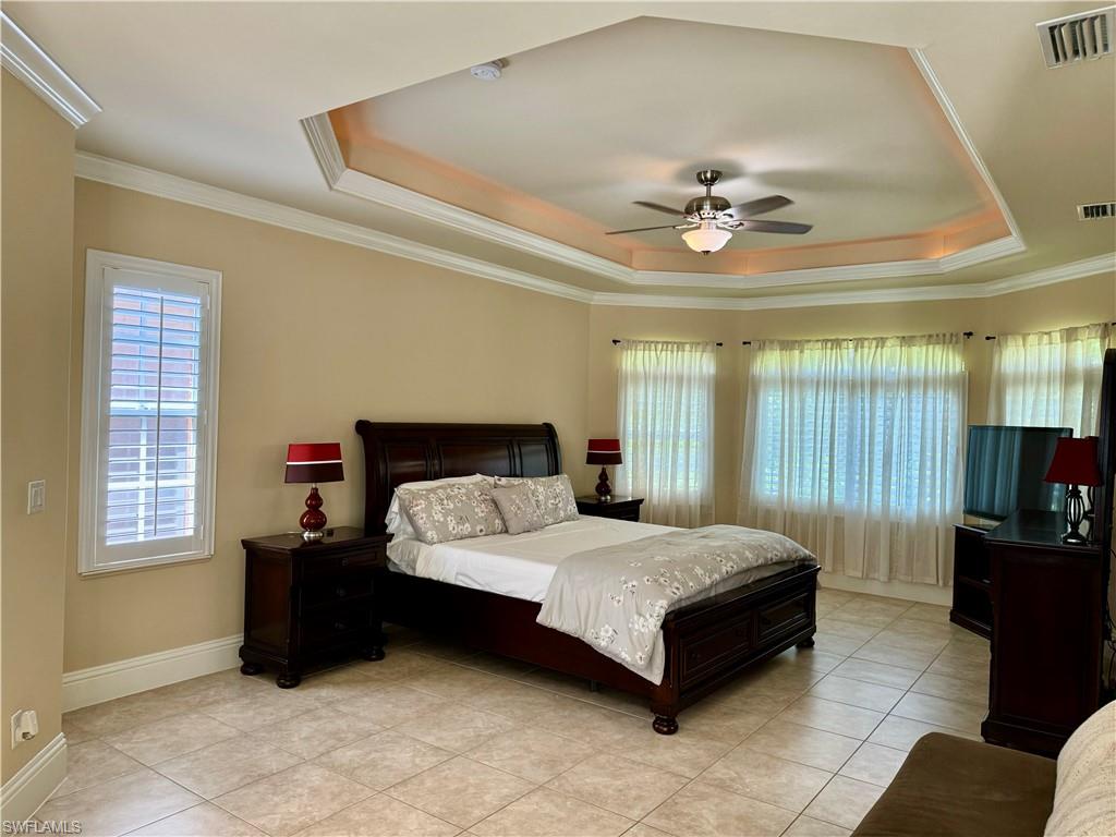 Bedroom featuring a ceiling fan, ornamental molding, multiple windows, light tile patterned floors, and a raised ceiling