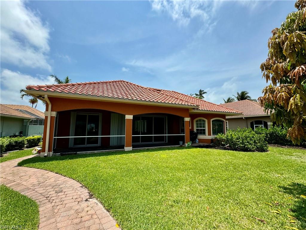 Back of property with stucco siding, a lawn, a tiled roof, and a sunroom
