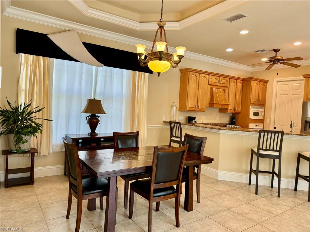 Dining space with crown molding, hanging lights, a ceiling fan, light tile patterned floors, and a tray ceiling