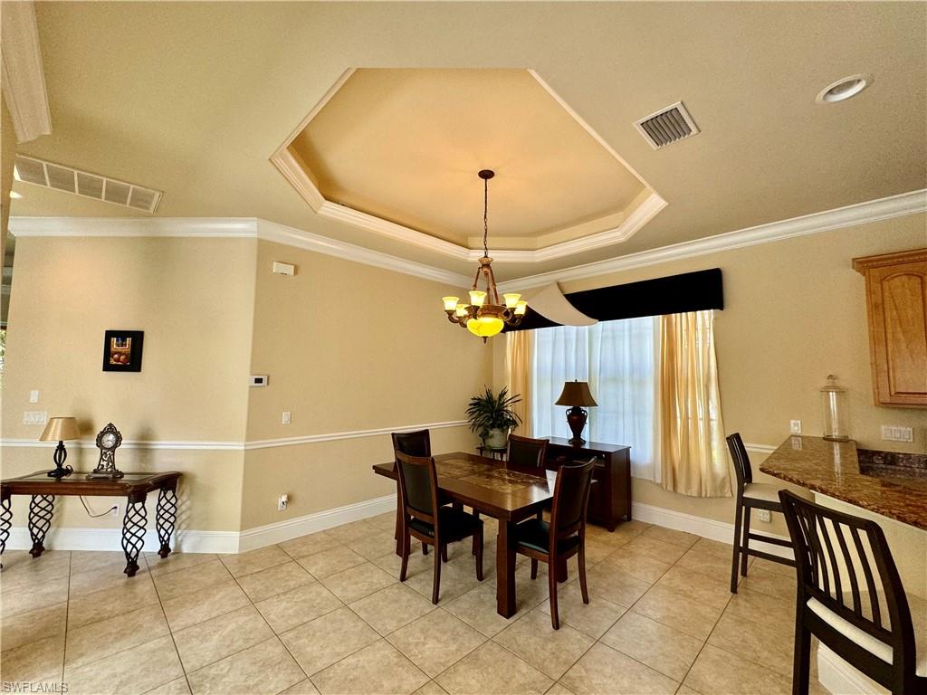 Dining area featuring hanging lights, crown molding, a tray ceiling, and light tile patterned flooring