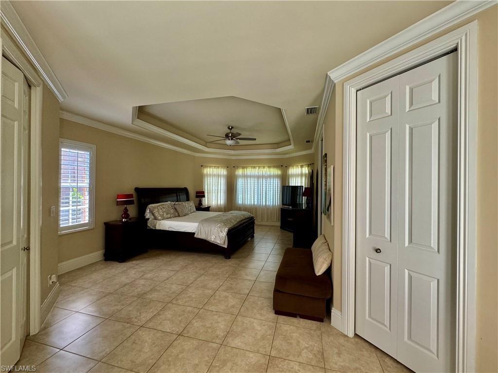 Bedroom featuring a tray ceiling, ornamental molding, light tile patterned floors, and a ceiling fan