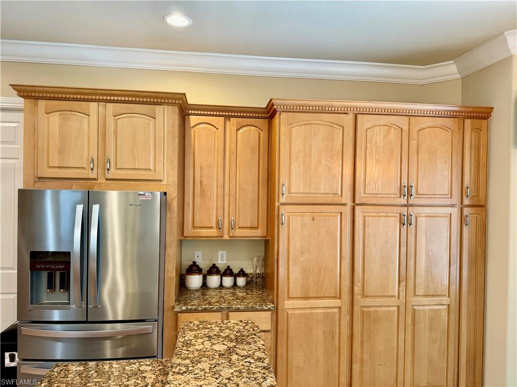 Kitchen with stainless steel fridge with ice dispenser, dark stone countertops, ornamental molding, and light wood finish cabinetry