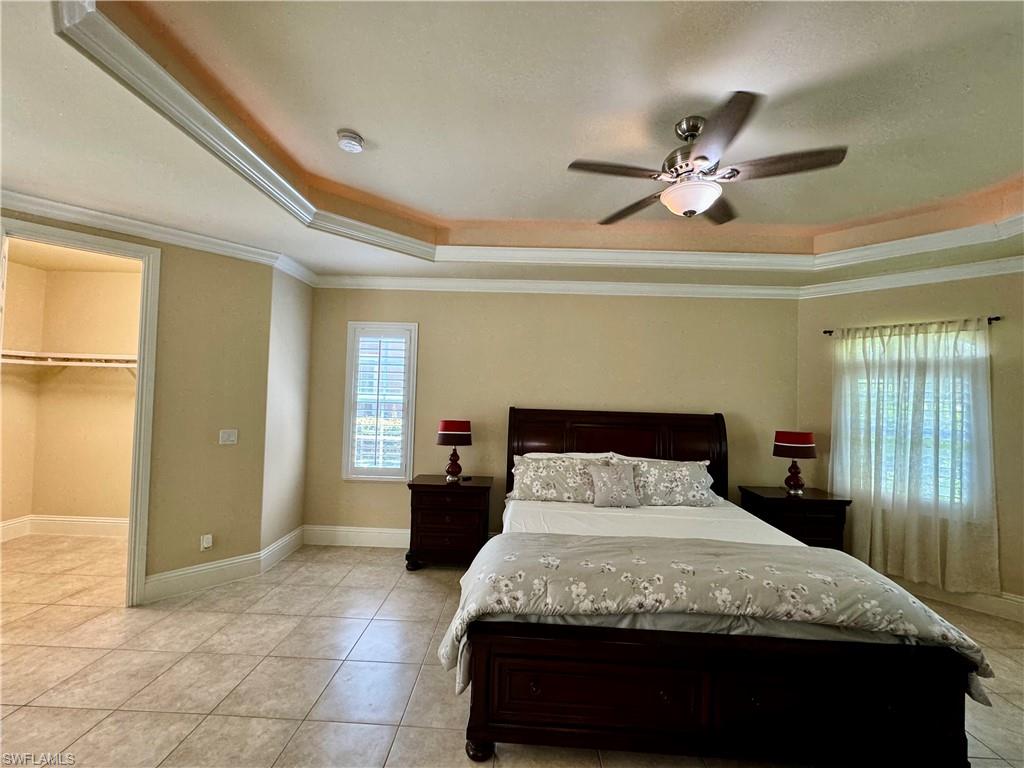 Bedroom featuring ornamental molding, a tray ceiling, a spacious closet, ceiling fan, and light tile patterned floors