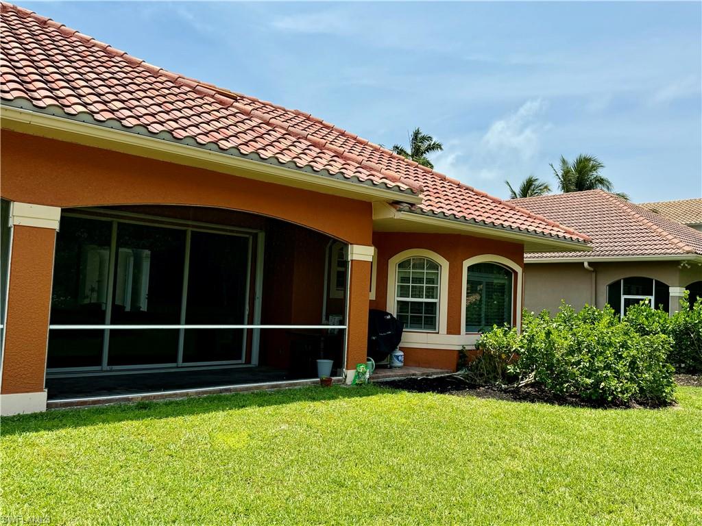 Rear view of property featuring a yard, stucco siding, a tiled roof, and a sunroom